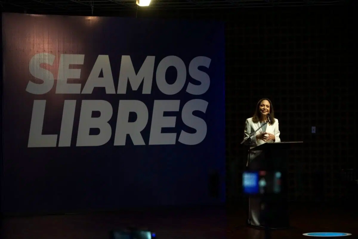María Corina Machado habla en el podio durante su primera rueda de prensa en la UCAB, con el lema «Seamos libres» al fondo