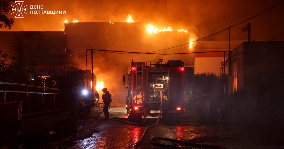 Bomberos y un camión de emergencias trabajan de noche frente a un edificio envuelto en llamas.