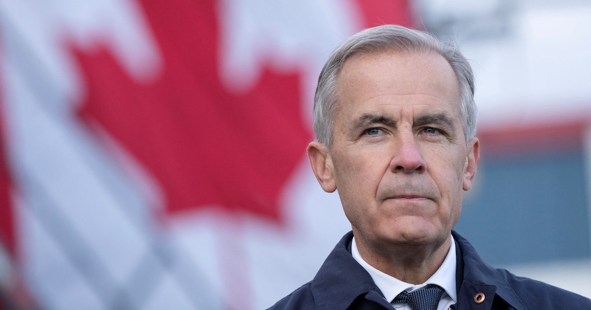 Hombre de cabello canoso y traje con una bandera desenfocada de Canadá de fondo.